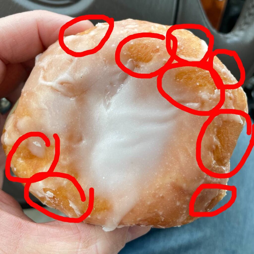 Donut with red circles around the edge depicting several areas that the glaze failed to cover.